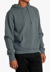 Sudadera con capucha en verde azulado apagado, hecha de tela suave. Cuenta con un bolsillo tipo canguro en la parte frontal y puños y dobladillo de canalé. Cuerda en la capucha.