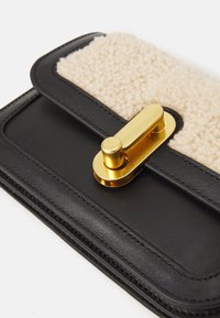 Svart läderplånbok med ett krämfärgat fleece-lock, säkrat med ett guldmetallspänne. Slät yta med sömdetaljer längs kanterna.