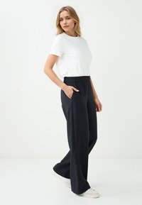 Schwarze, locker sitzende Hosen mit einem elastischen Bund, seitlichen Taschen, kombiniert mit einem schlichten weißen T-Shirt und weißen Turnschuhen.
