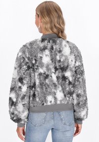 Donna che indossa una giacca fuzzy grigia e bianca con polsi e orlo a coste, abbinata a jeans azzurri, vista da dietro.