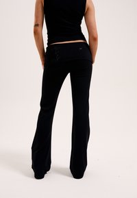 Pantaloni neri a palazzo con una texture morbida, caratterizzati da un design decorativo in vita e una silhouette aderente che si allarga alla caviglia.