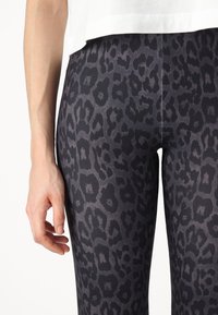 Črne legice z sivo leopardjim vzorcem. Narejene iz elastičnega materiala, s prilegnjenim dizajnom in gladko teksturo.