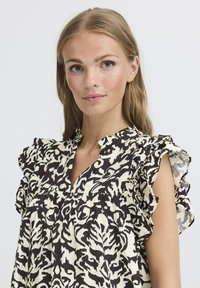 Blusa nera e crema con volant e design a motivo, caratterizzata da scollatura a V e tessuto leggero; maniche corte con volant.