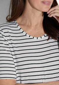 Weißes Shirt mit schwarzen horizontalen Streifen, rundem Halsausschnitt, kurzen Ärmeln und weicher Textur, fokussiert auf minimalistisches Design und Muster.