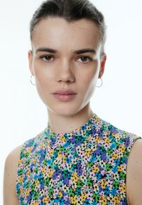 Ärmelloses Top mit Blumenmuster und hohem Kragen, aus leichtem Stoff in lebhaften Farben wie Lila, Gelb, Grün und Blau.