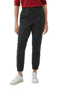 Pantalon de jogging noir avec poignets élastiques et taille à cordon de serrage. Doté de poches latérales et d'un tissu en mélange de coton lisse. Style avec des baskets blanches.
