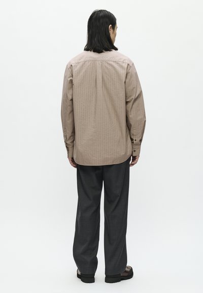 Camisa de botones a rayas marrón con dobladillo curvado, combinada con pantalones de pierna ancha gris oscuro y sandalias negras. Tejido suave, corte relajado.