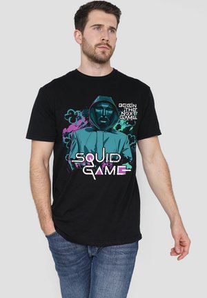 Schwarzes Baumwoll-T-Shirt mit einem grafischen Design eines Charakters mit Kapuze, Text mit der Aufschrift "BEGIN THE NEXT GAME" und "SQUID GAME" in lebhaften Farben.