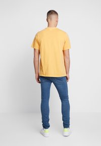 Camiseta de algodón amarilla con mangas cortas, cuello redondo y un corte holgado, combinada con jeans ajustados azules y zapatillas blancas con acentos en neón.