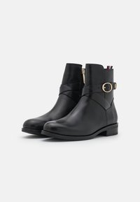 Botas de cuero negras hasta el tobillo con punta redonda, cremallera lateral, detalle de hebilla y tacón bajo. Textura suave con un brillo sutil.