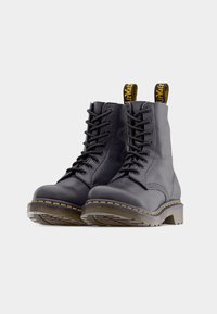 Bottes en cuir noir à lacets avec un bout arrondi, des coutures jaunes et des languettes de traction. Semelle en caoutchouc robuste. Partie supérieure texturée avec une finition mate.