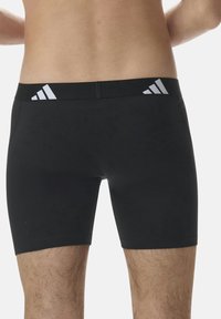 Svarta shorts i stretchmaterial med en mjuk yta. Har vita Adidas-logostråk på midjebandet. Längd till mitten av låret.