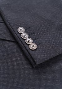 Dark gray patterned suit fabric with a smooth texture, featuring four metallic buttons with engraved branding along the cuff.