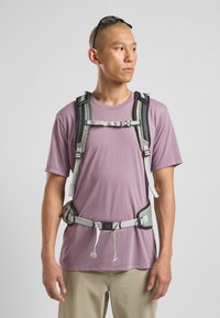 Lightweight, gray adjustable harness with padded straps and buckles, worn over a short-sleeve lavender shirt, worn by a person against a neutral background.