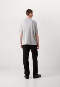 Gray short-sleeve T-shirt with a round neckline, relaxed fit, paired with black straight-leg pants and black footwear. Tattoo visible on forearm.