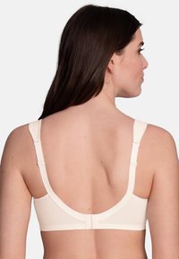 Soutien-gorge beige en tissu lisse, avec une large bande, des bretelles ajustables et une fermeture à crochet et œillet au dos. Design minimaliste, finition sans couture.