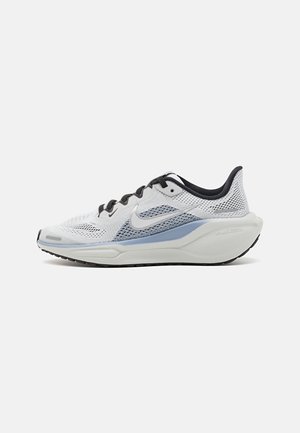 Zapatilla de correr en gris claro y azul con cordones negros, parte superior de malla transpirable y suela gruesa con amortiguación, sobre un fondo blanco liso.