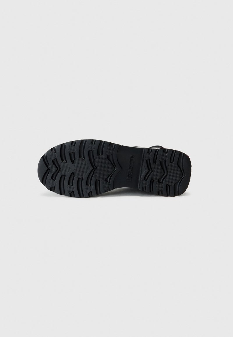 Sole di scarpa in gomma nera con scanalature profonde e una superficie testurizzata, caratterizzata da un profilo curvo e pattern stampati per la trazione.