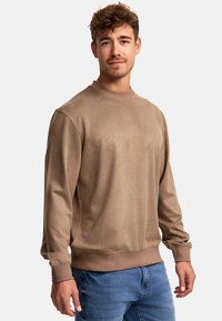 Bruine crewneck sweater met lange mouwen, gemaakt van zachte stof, met ribgebreide manchetten en zoom, gecombineerd met blauwe spijkerbroek.