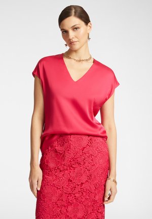 Top di raso fucsia con scollo a V e maniche corte, abbinato a una gonna in pizzo testurizzato con motivi floreali in un colore coordinato.