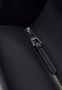 Černé kožené kotníkové boty s kovovým zipem a logem, hladkým povrchem a minimalistickým designem.