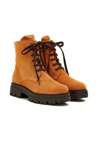 Botas de tobillo de ante en color marrón claro, con cordones marrones y una suela de goma negra gruesa. Los lados tienen texturas suaves con acentos mínimos.