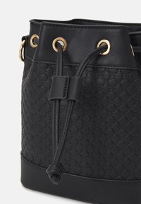 Czarna torba typu bucket wykonana z teksturowanego materiału syntetycznego. Wyposażona w złote oczka i zapięcie na sznurek. Ustrukturyzowany design z solidnym dnem.