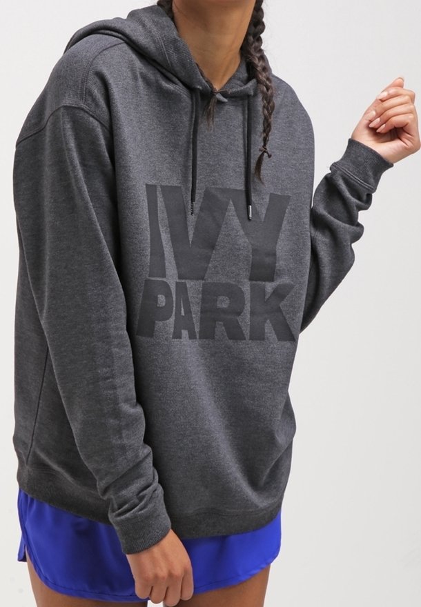 Personne portant un sweat à capuche IVY PARK gris foncé et un short bleu vif, avec des cheveux tressés, sur un fond clair uni.