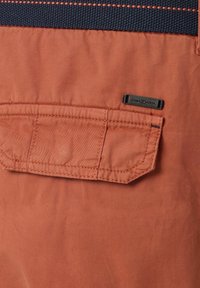 Pomarańczowa tkanina o gładkiej fakturze, z przeszywaną kieszenią i ciemnoniebieskim akcentem wplecionym. Metka z napisem "CASA MODA" na czarnej etykiecie.