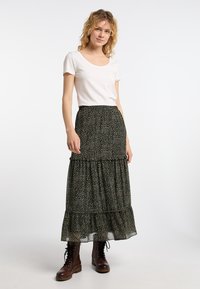 Schwarze Blumen-Maxirock mit gestuften Rüschen, aus leichtem Stoff gefertigt. Kombiniert mit einem schlichten weißen T-Shirt und braunen Schnürstiefeln.