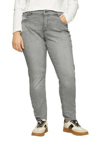 Graue Jeans aus Denim mit geradem Schnitt, Fünf-Taschen-Design und Gürtelschlaufen. Kombiniert mit weißen und sandfarbenen Sneakers mit schwarzen Akzenten.