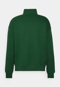 Sweat-shirt vert foncé avec un col montant, des manches longues, des épaules tombantes et des poignets côtelés. Tissu à finition lisse, design minimaliste.