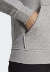 Grå sweatshirt med känguruficka, ribbade ärmslut och en mjuk textur. Höjdpunkterna inkluderar sydda sömmar och en lös fåll.