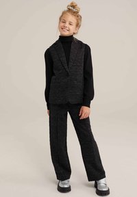 Svart strukturerad väst och byxor-set med en enkel knappstängning, ribbad turtleneck och glänsande silverfärgade skor med tjock sula.