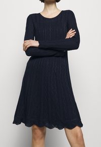 Náměstní modré šaty s dlouhým rukávem, texturovanými diamantovými vzory, zvlněným lemem a kulatým výstřihem. Měkká látka s volným střihem.
