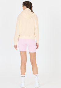 Beige Kapuzenpullover und rosa Radshorts. Der Pullover hat einen lockeren Schnitt, während die Shorts glatt und enganliegend sind.