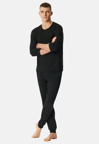 Zwarte langemouwen shirt met een zak en bijpassende broek. Gemaakt van een gladde stof, met een ontspannende pasvorm en taps toelopend beenontwerp.