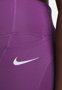 Leggings deportivos púrpuras con un tejido suave y elástico. Presentan un logotipo blanco de Nike y un diseño de costuras único cerca de la cintura.