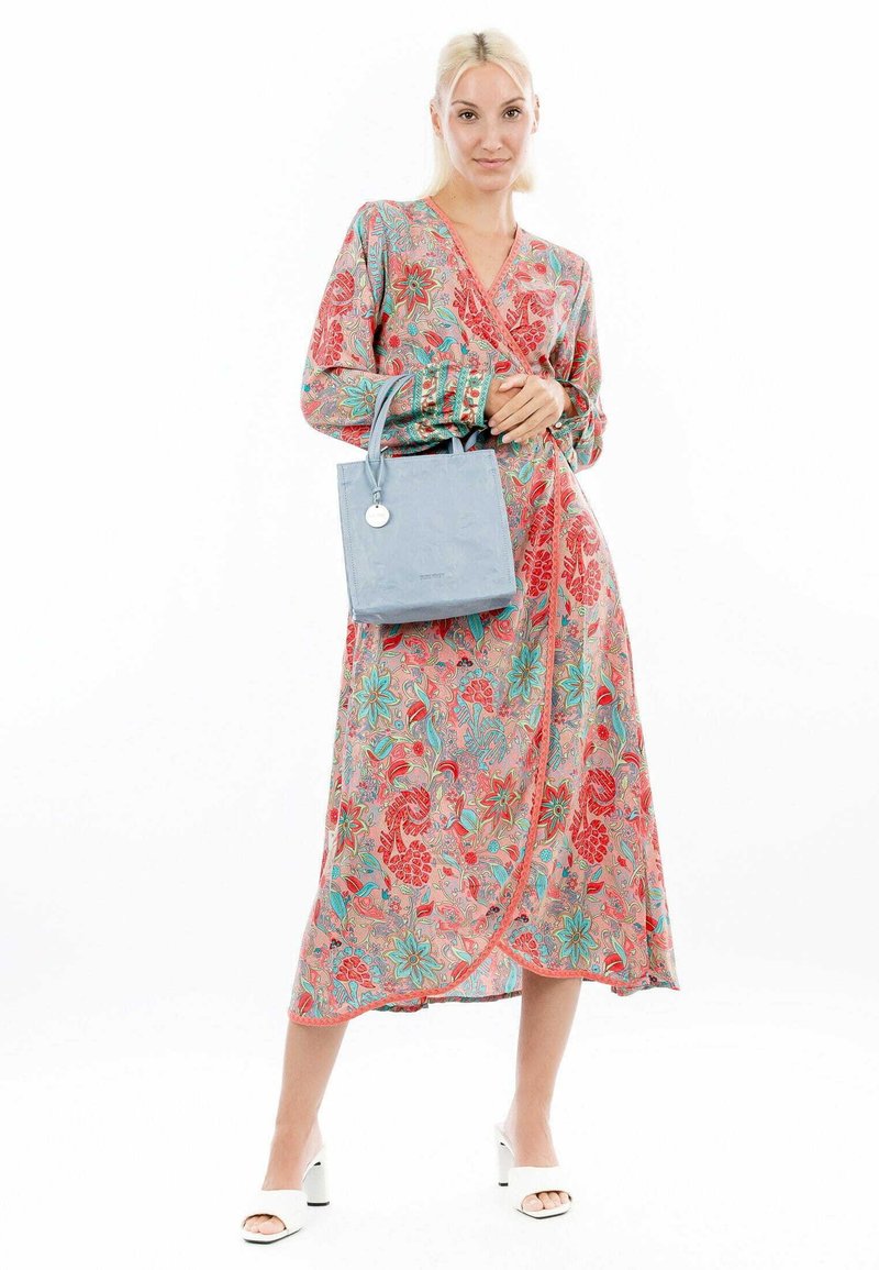Floral wrap dress featuring red and turquoise designs on a pink background. Paired with a light blue tote bag and white block-heeled sandals.