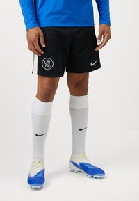 Sorte Nike shorts med hvide sidestropper, prydet med et cirkulært klublogo. Hvide knæ-lange sokker og blå-hvide fodboldstøvler.
