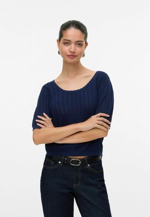 Mörkblå stickad tröja med ribbat mönster, vid båturringning och korta ärmar, baren med mörka jeans och ett svart bälte.