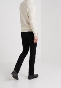 Cream cable-knit sweater, black slim-fit jeans, and black leather shoes. Sweater has high neckline; jeans feature back pockets and minimal detailing.
