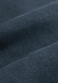 Tejido de algodón azul oscuro con un patrón texturizado y acanalado, que muestra variaciones sutiles en color y trama. Textura suave y lisa visible.