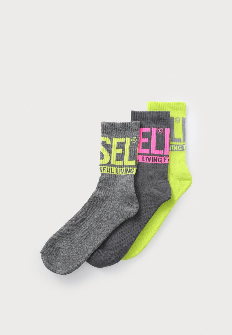 Tres calcetines en gris, gris oscuro y verde neón. Cada uno presenta un diseño acanalado y un texto en negrita. El material parece suave y elástico.