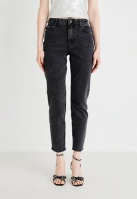 Svart denim jeans med smal passform, høy midje og oppbrettede ben, kombinert med svarte stroppelivhæler med sløyfer og perle detaljer.
