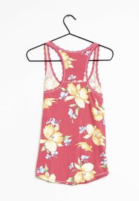 Röd ärmlös blommig linne med gula och ljusblå blommor som hänger på en svart klädhängare mot en vit bakgrund.