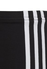 Black textile featuring three vertical white stripes. The fabric has a smooth texture, with ribbing along the edges of the stripes.