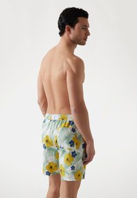 Șorturi de baie pentru bărbați cu un model floral galben și albastru pe un fundal verde deschis. Talie elastică cu branding pe spate.