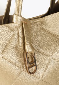 Zbliżenie na lśniącą złotą torebkę, wyposażoną w teksturowaną skórę i metalowy zamek, ukazującą szczegółowe detale i rzemiosło.