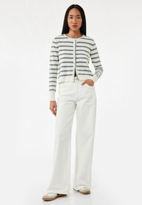 Witte gestreepte cardigan met grijze strepen, sluiting met knopen aan de voorkant en geribde manchetten, gecombineerd met wijde witte jeans. Casual ontwerp en pasvorm.